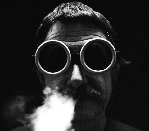 A portrait of Ettore Sottsass wearing goggles and blowing smoke