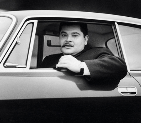 A portrait of Joe Colombo smoking a pipe inside his car